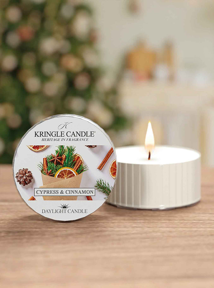 Kringle Candle Cypress & Cinnamon candle on a table with a blurred Christmas tree in the background