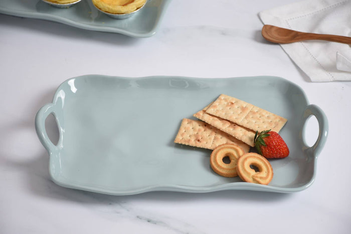 Light blue ceramic tray with crackers, cookies, and a strawberry on a white surface.