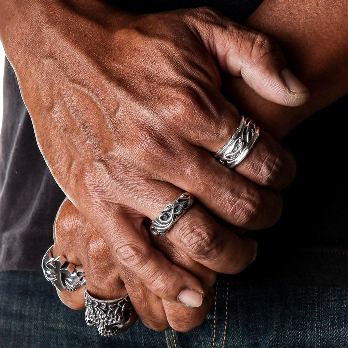 A man wearing the tribal silver band ring on his finger, styled with other biker rings.