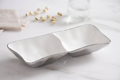 Silver serving dish on a white surface with small decorative items.
