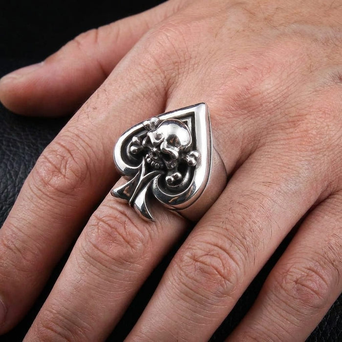Silver spade and skull biker ring worn on a man's hand against dark leather.