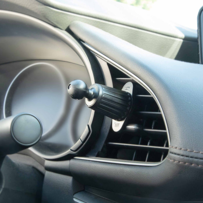 A close-up of a modern dashboard features an Adjustable Car Vent Mount with 17mm Ball, shown with a small black cylindrical air freshener attached to the vent slats and the device holder on the mounts base.