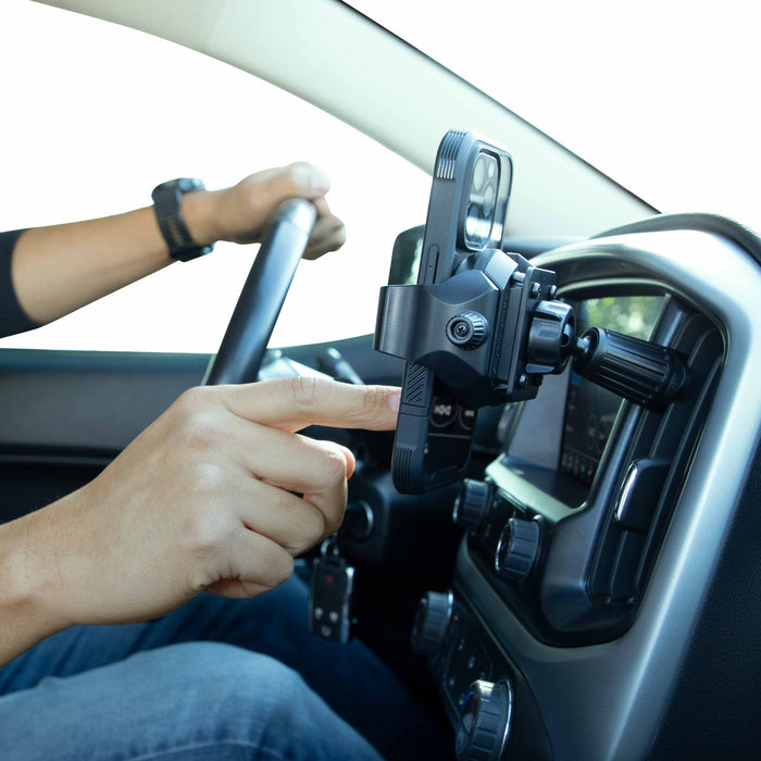 A driver uses their right hand to adjust a smartphone in an Adjustable Car Vent Mount with 17mm Ball on the dashboard, while keeping their left hand on the wheel for safer, hands-free phone use.