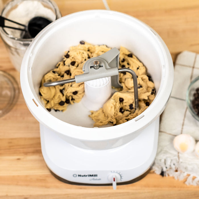 Top view of a NutriMill artiste mixer mixing chocolate chip cookie dough on a wooden surface