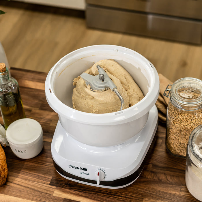 NutriMill artiste mixer mixing dough on a wooden counter next to salt, grains, and oil