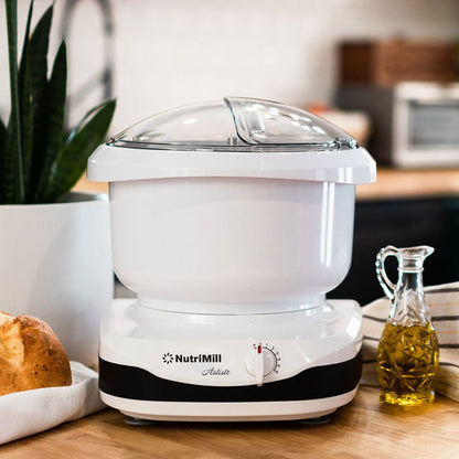 NutriMill artiste mixer on a wooden counter next to bread and oil with a blurred background