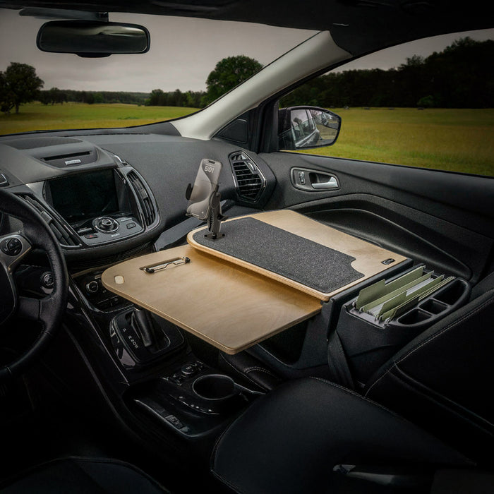 The car interior is transformed into a functional mobile office workstation with the AutoExec GripMaster Car Desk featuring a Mega Grip™ Drill-Base Mount, securely positioned over the passenger seat to hold a clipboard, mouse pad, files, and phone—set against the scenic backdrop visible through the windows.