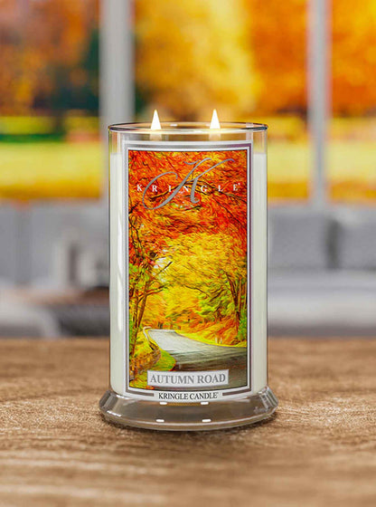 Kringle Candle with 'Autumn Road' design on a wooden surface with blurred autumn-themed background