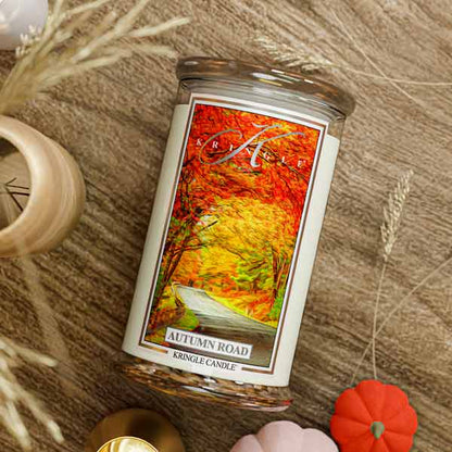 Kringle Candle with 'Autumn Road' design on a wooden surface with blurred autumn-themed background
