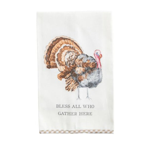 An off-white kitchen tea towel featuring a watercolor-style turkey illustration and the printed phrase 'BLESS ALL WHO GATHER HERE' near the bottom, with a beige-and-white gingham border along the lower edge.