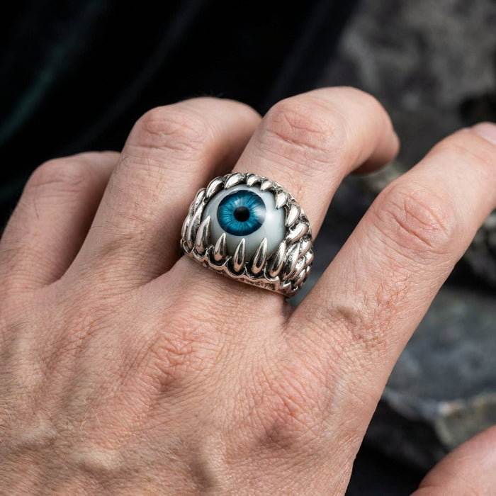 Silver monster eyeball ring with realistic blue iris surrounded by claw-like prongs worn on a man's finger, gothic biker jewelry style