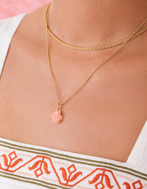 Close-up of a person wearing a gold necklace with a shell pendant, against a blurred background.