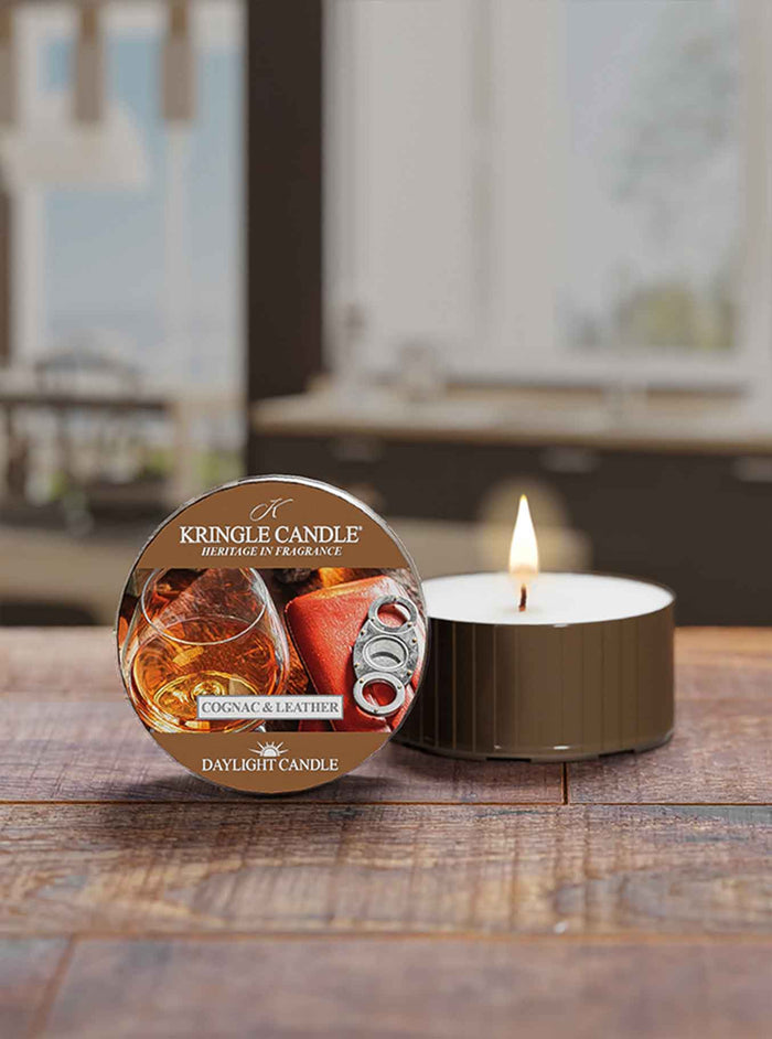 Kingle Candle Cognac & Leather daytime candle on a wooden surface with a blurred background