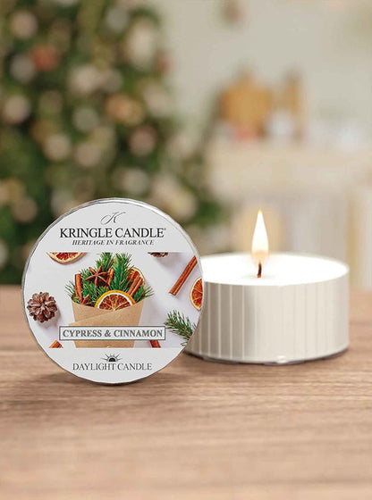 Kringle Candle Cypress & Cinnamon candle on a table with a blurred Christmas tree in the background
