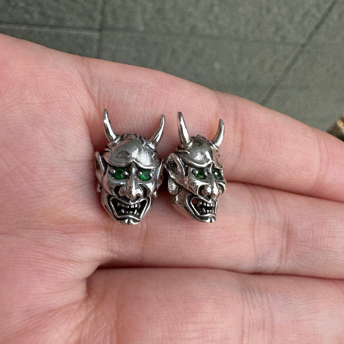 An angled view of the Japanese demon stud earrings, showing the 3D detail and green eyes.