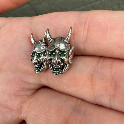 The pair of handmade green-eyed devil earrings shown together in a person's palm.