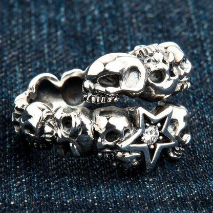 Detailed view of the overlapping silver band resting on denim, emphasizing the carved skulls and jeweled star centerpiece.