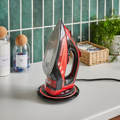 Red and black iron on a white surface with a tiled wall and plants in the background