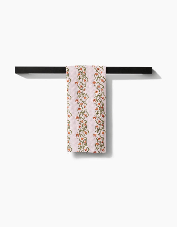 Decorative towel with floral pattern hanging on a black shelf against a white background