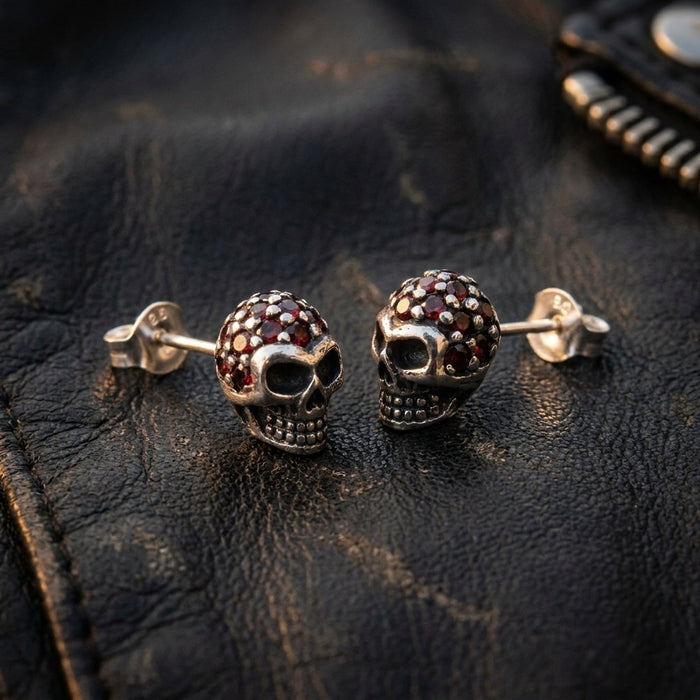 Pair of garnet crown skull studs resting on a black leather biker jacket, butterfly backs alongside