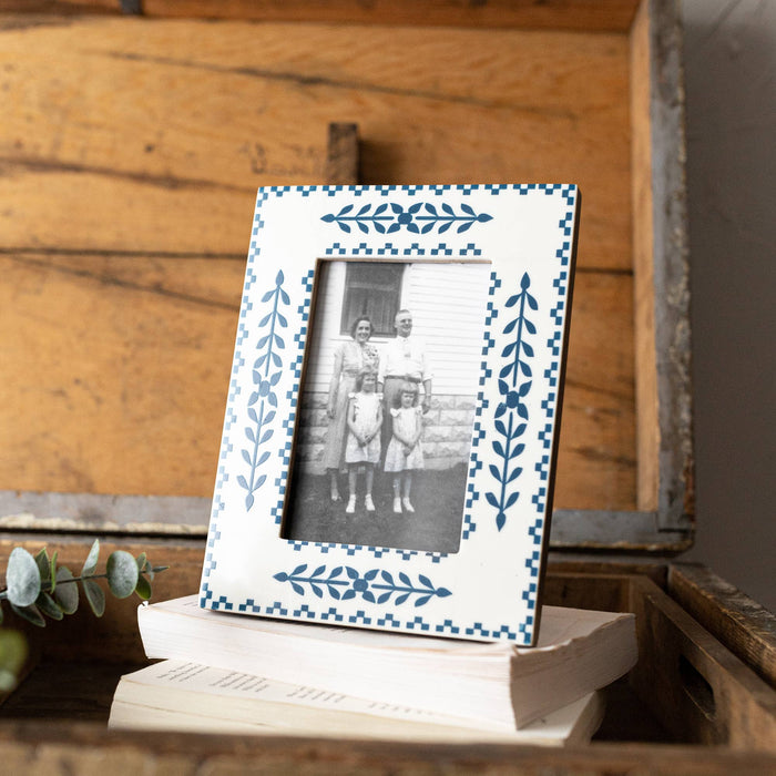 A 4x6 picture frame with a blue botanical pattern printed over white resin, displayed on a wooden surface with a photo of two individuals inside the frame.