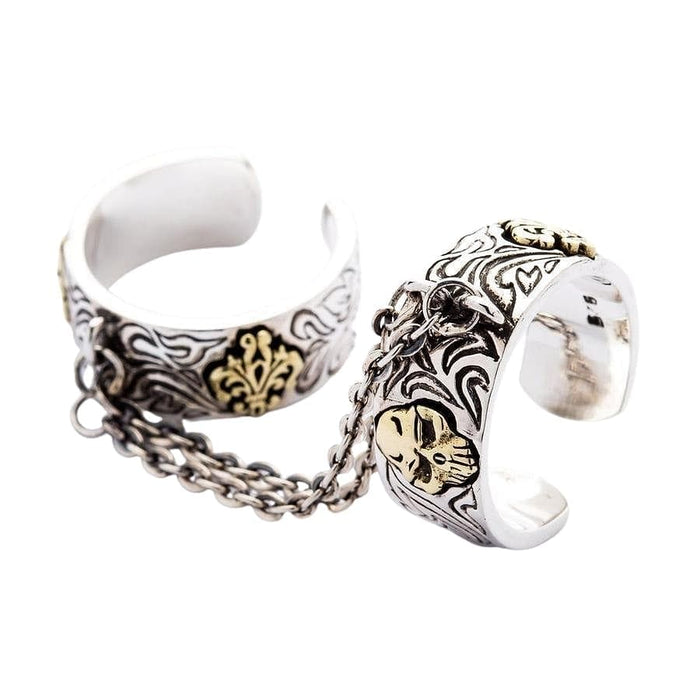 An angled view of the goth chained two finger ring, showing the sterling silver bands, brass skulls, and connecting chain.