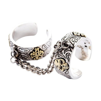 An angled view of the goth chained two finger ring, showing the sterling silver bands, brass skulls, and connecting chain.