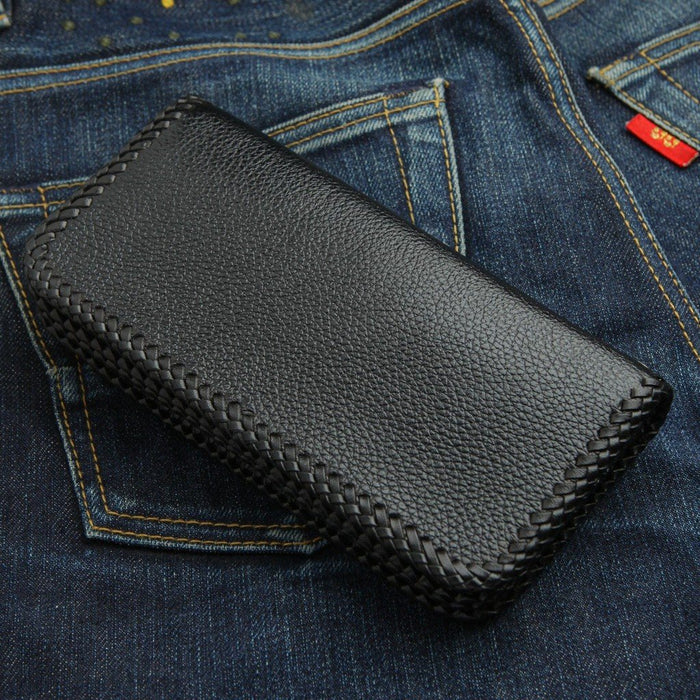 Reverse side of the black pebbled leather wallet lying on denim, emphasizing the continuous braided edge stitching.