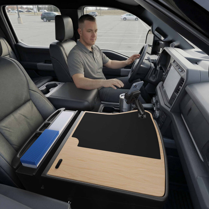A man sits in the driver’s seat of a parked vehicle, using the GripMaster Efficiency Car Desk with Mega Grip™ Drill-Base Mount as a spacious mobile workstation, with organized files on the front passenger seat.