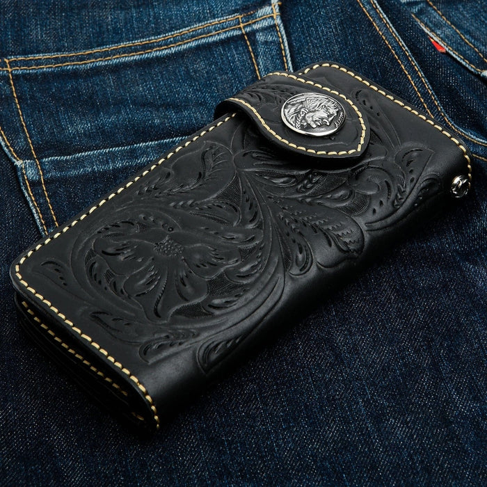 A black leather trucker wallet with Western floral tooling resting on a pair of denim jeans.