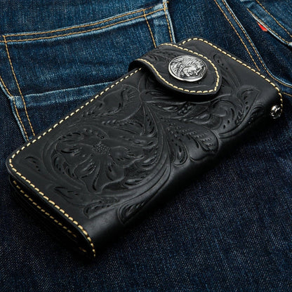 A black leather trucker wallet with Western floral tooling resting on a pair of denim jeans.