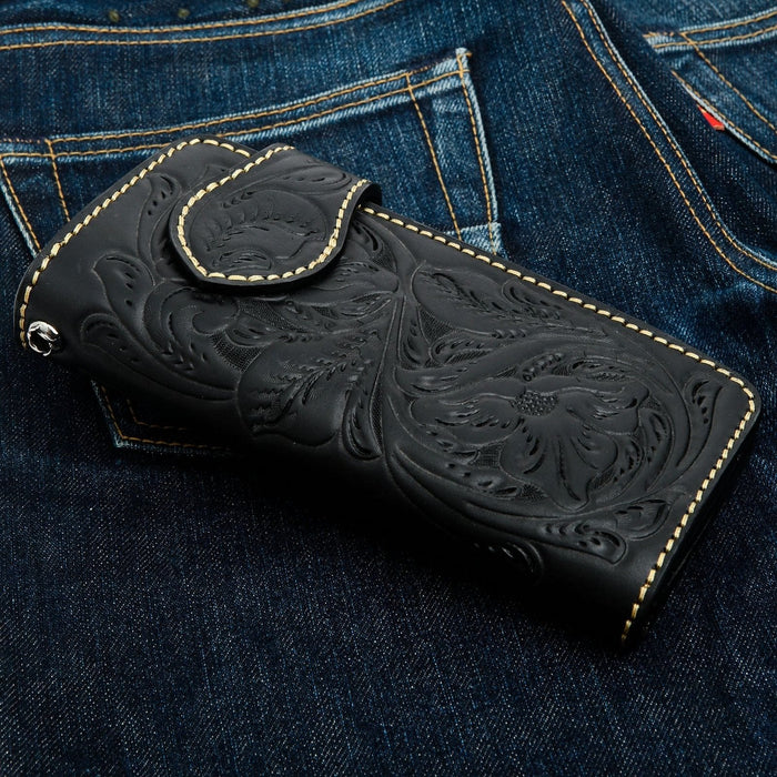 Floral and leaf tooling pressed into black cowhide, pale stitching outlining the panel against dark denim.