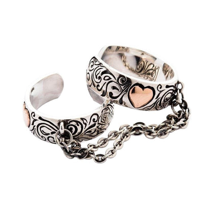 An angled view of the heart chained two finger ring, showing the sterling silver bands, rose gold hearts, and connecting chain.