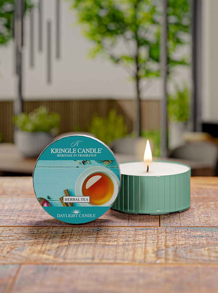 Kingle Candle labeled 'Herbal Tea' on a wooden surface with a blurred indoor background