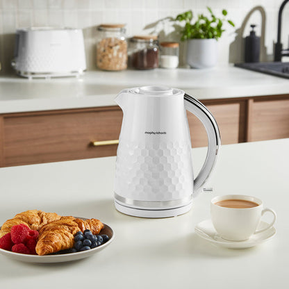 White electric kettle on a kitchen counter with a plate of pastries and a cup of coffee.