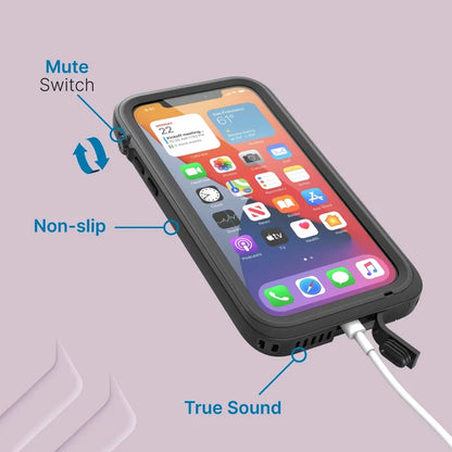 An iPhone 12 with a Catalyst Case US waterproof, total protection case in rugged black displays its home screen. Blue labels highlight the mute switch, non-slip edge, and charging cable by a "True Sound" vent on a light purple background.