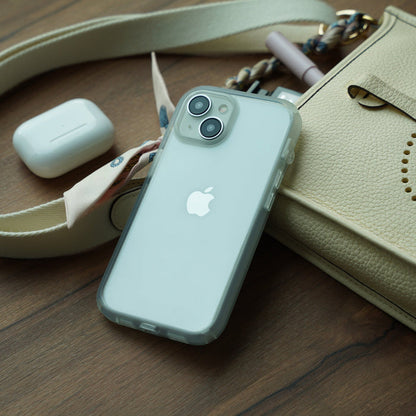 A Catalyst Case US iPhone 16 Plus with the clear Influence Case rests on a wooden surface beside a cream purse, scarf-detailed strap, and closed white AirPods case, creating a tidy and stylish scene.