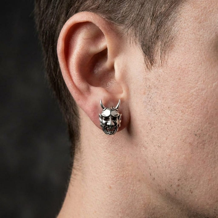 Lifestyle shot of the sterling silver Japanese demon mask earring worn on a model's earlobe to demonstrate scale and fit.