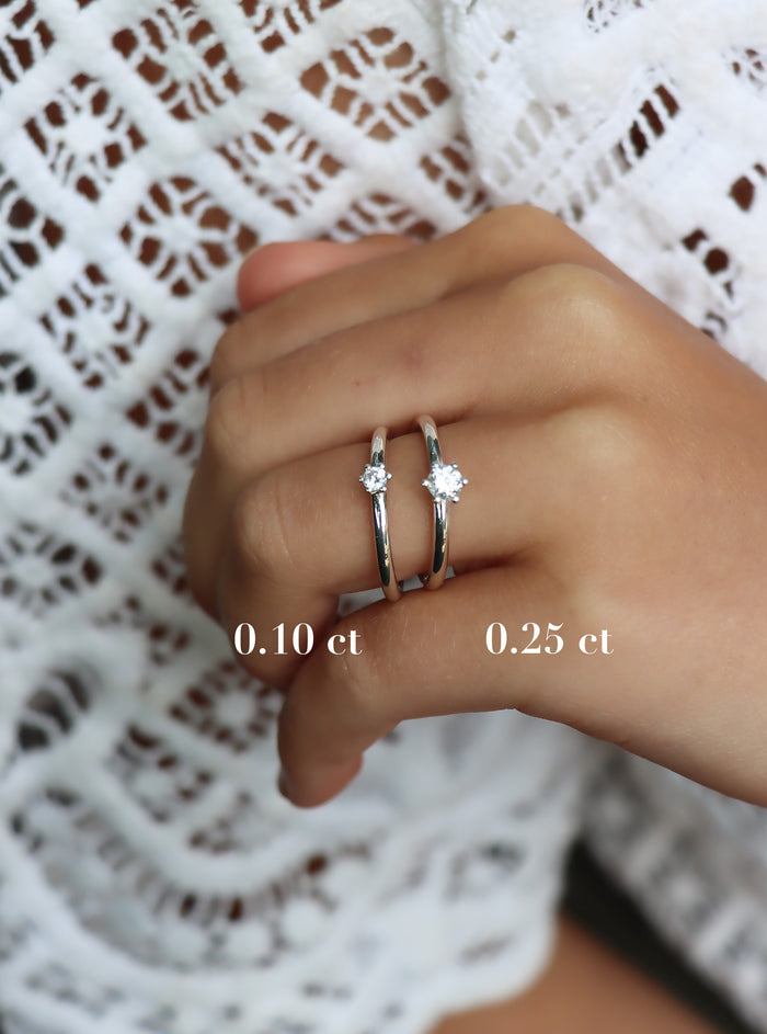 Tjej som bär två diamantringar för att visa storleken på de olika diamanterna. En ring har 0,10 ct diamant och en ring har 0,25 ct diamant.