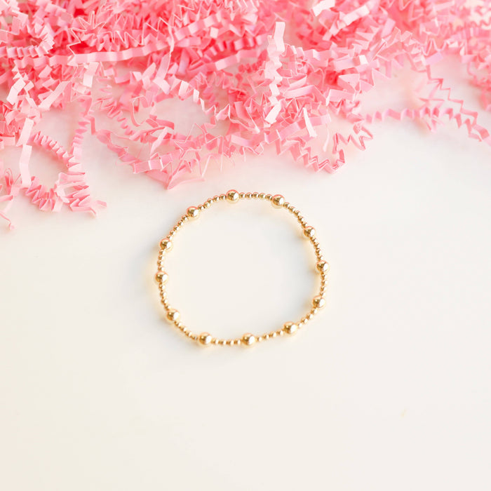 Gold beaded bracelet on a white background with crumpled pink paper