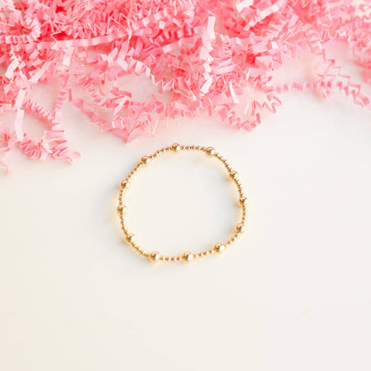 Gold beaded bracelet on a white background with crumpled pink paper