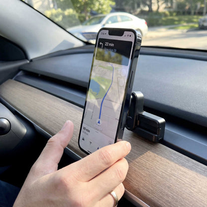 A hand holds a smartphone in a car mount on the dashboard, displaying a GPS navigation map with route guidance—seamlessly paired with the Magnetic Phone Vent Mount for Tesla Model 3 (2017–2022) and Model Y (2020–2023) for secure and convenient navigation.