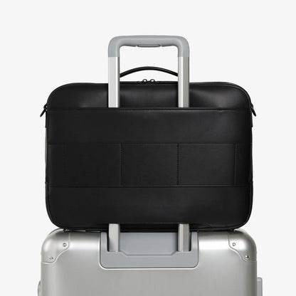 Carbon Black (Vegan Leather) | Back view of Metro Briefcase in Carbon Black with trolley sleeve attached to a silver suitcase handle