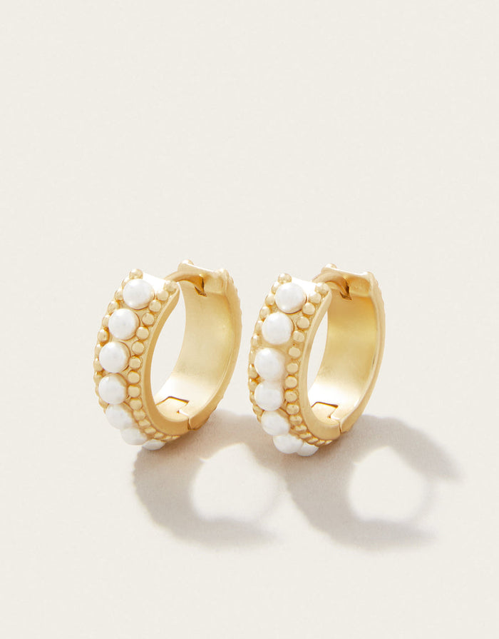 Gold hoop earrings with white bead accents on a light beige background
