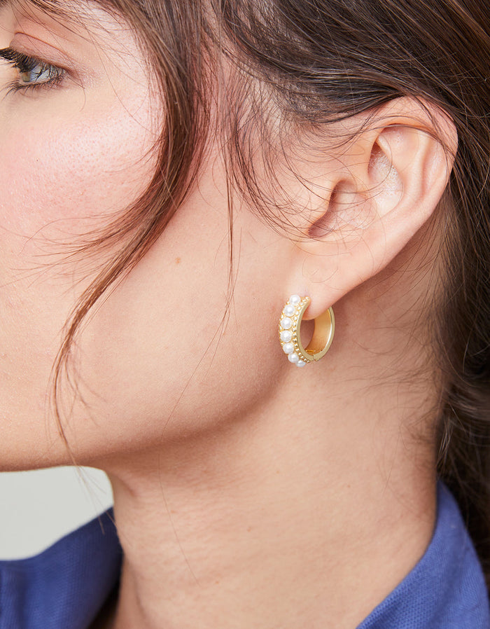 Close-up of a person wearing gold hoop earrings with a blurred background