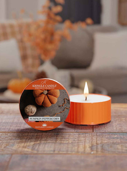 Orange candle with packaging labeled 'Pumpkin Peppercorn' on a wooden surface.