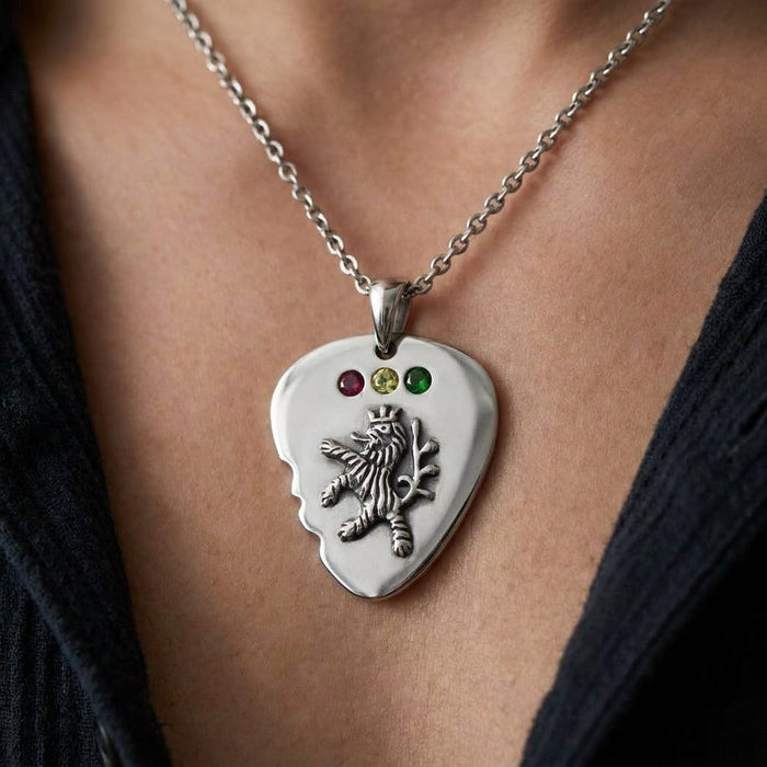 A person wearing a silver guitar pick pendant necklace featuring an embossed lion and three small red, yellow, and green stones.