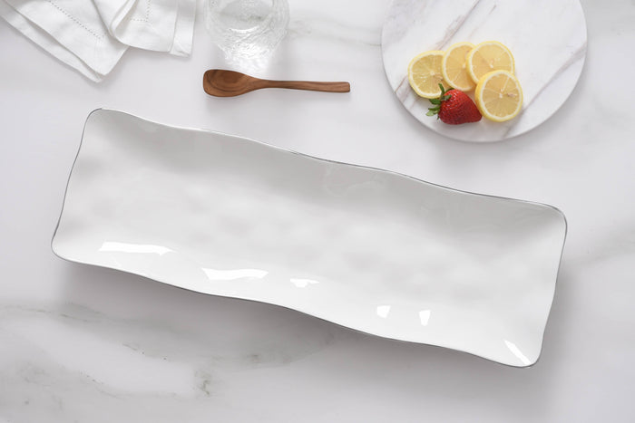 Rectangular white ceramic platter on a marble surface with a plate of fruit in the background.