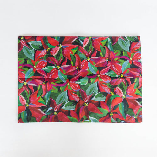 A reversible placemat featuring a vibrant, original Kim Hovell artwork with a Poinsettia pattern.