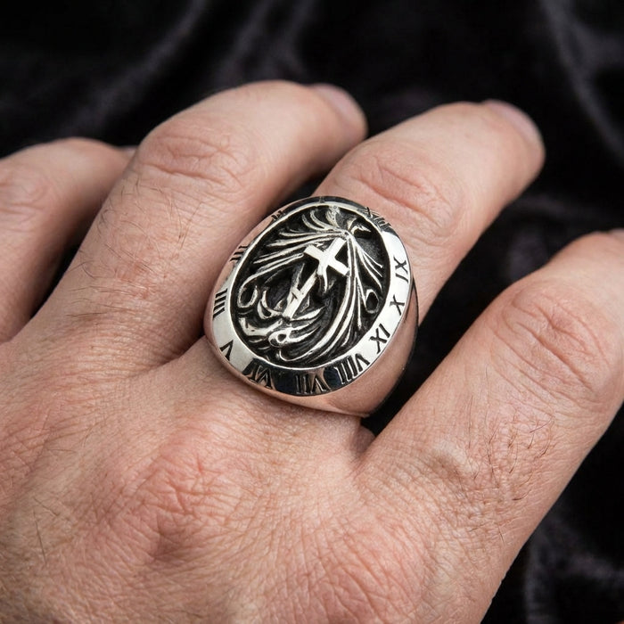 Close-up of a men's sterling silver gothic signet ring worn on a hand, featuring a central cross design with flame details surrounded by an engraved Roman numeral bezel against a dark background.